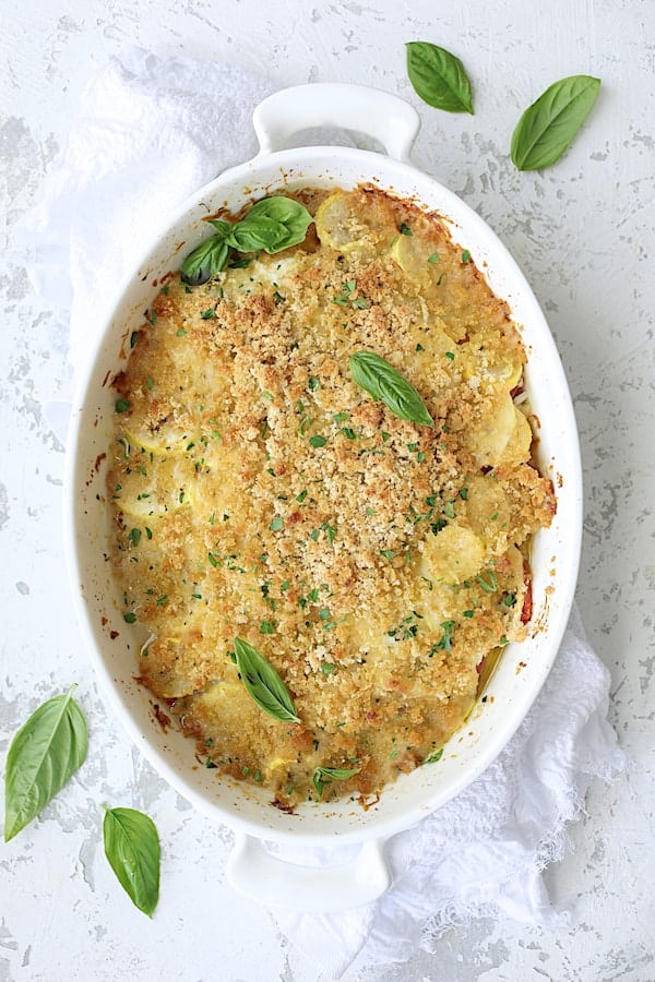 Photo of baked Yellow Squash and Tomato Gratin with Two Cheeses on white distressed background with white towel.