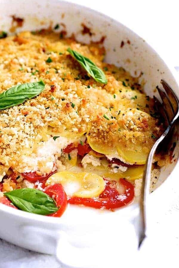 Yellow Squash and Tomato Gratin in oval white baking dish with piece removed.