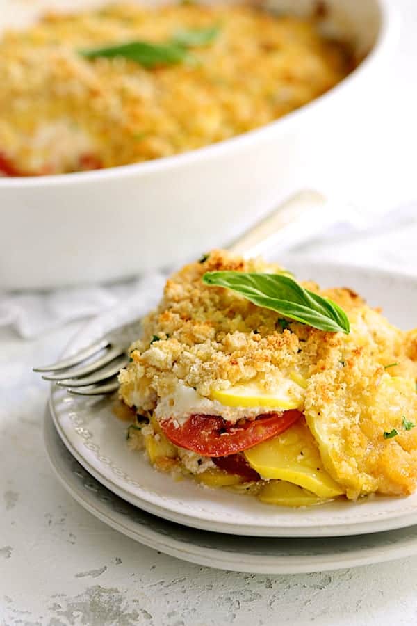 Close-up photo of a serving of Yellow Squash and Tomato Gratin with Two Cheeses on white plate.