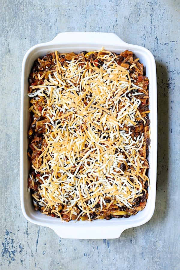 Photo of casserole in white baking dish with cheese added before being baked.