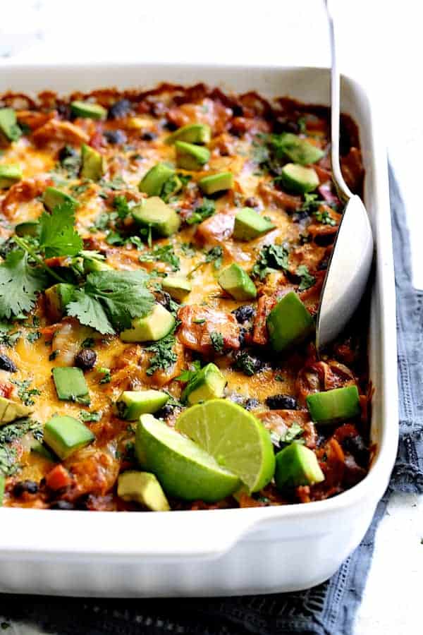Photo of baked Black Bean and Yellow Squash Enchilada Casserole with serving spoon garnished with lime wedges and cilantro sprigs.