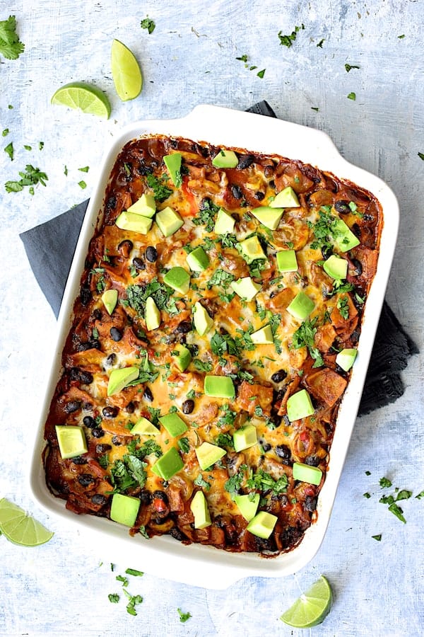 Photo of Black Bean and Yellow Squash Enchilada Casserole in white ceramic baking dish on pale blue background.