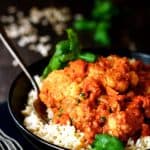 Cauliflower and Sweet Potatoes in Roasted Red Pepper Mole over rice in black bowl.