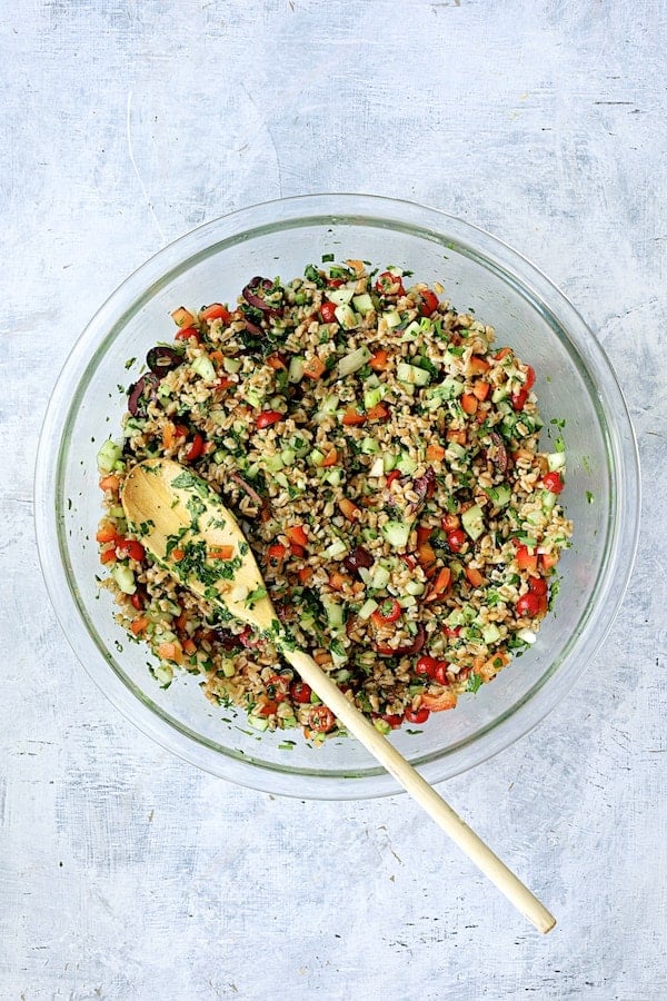 Photo of salad in glass mixing bowl mixed together with white spoon.