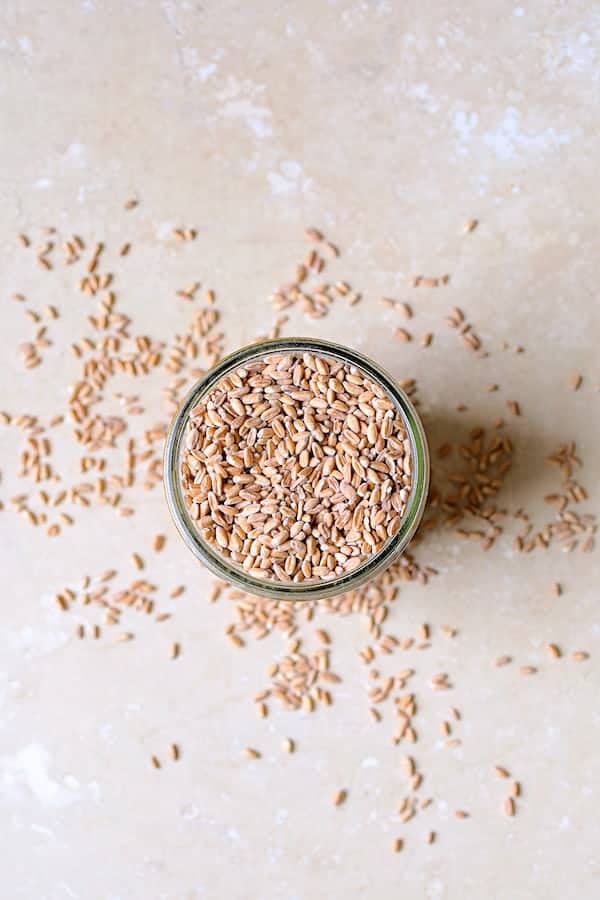 Photo of uncooked farro in glass jar on marble background.