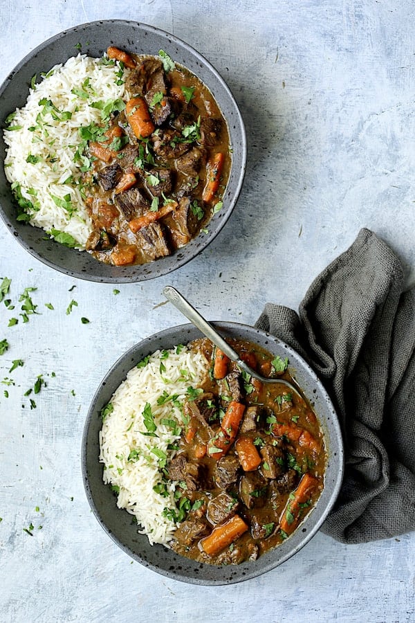 Photo of two servings of Pressure Cooker Indian Curry Beef Stew with white basmati rice on pale blue background with dark gray napkin.