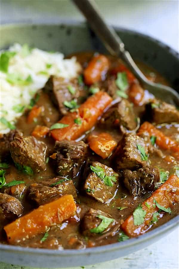 Close-up photo of one serving of Pressure Cooker Indian Curry Beef Stew in gray bowl.