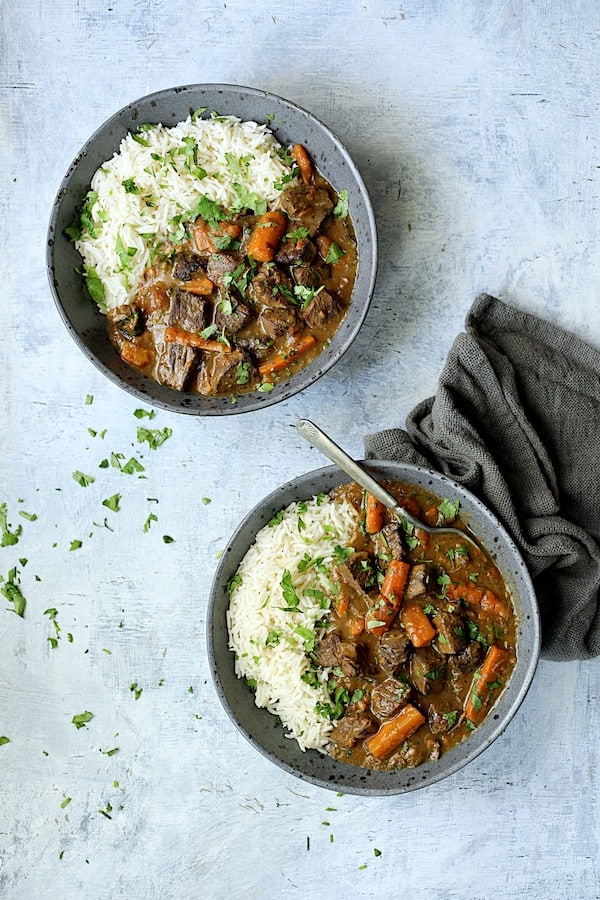 Photo of two servings of Pressure Cooker Indian Curry Beef Stew in gray bowls on pale blue background garnished with cilantro.