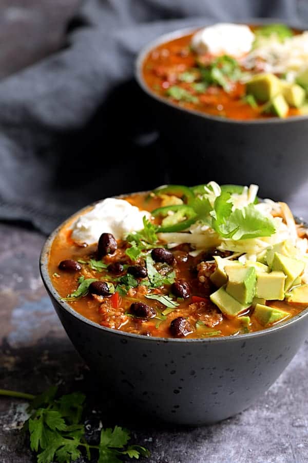 Turkey, Black Bean and Quinoa Chili - Chili served up in gray bowls garnished with sour cream, cheese, avocado, jalapeno and cilantro