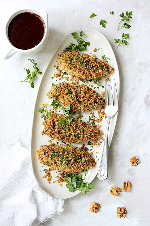 Walnut-Crusted Chicken with Pomegranate Sauce - Overhead shot of dish on white platter with sauce on marble background garnished with parsley