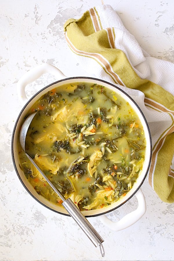 Photo of the pot of Cold-Fighting Chicken Soup with Kale and Orzo in white Dutch oven with soup ladle.