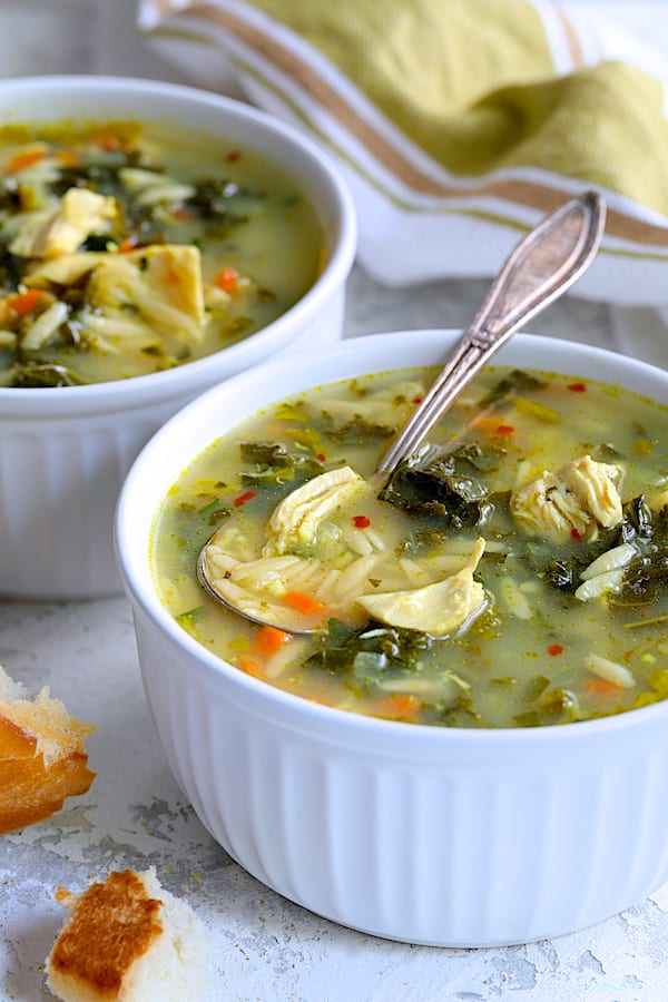 Close-up photo of a serving of Cold-Fighting Chicken Soup with Kale and Orzo in white bowls with spoon.
