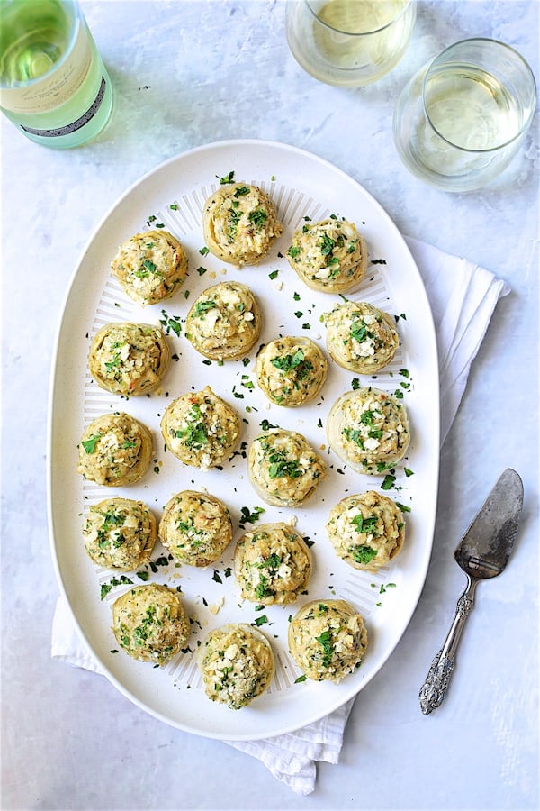 Photo of Deviled Crab-Stuffed Artichoke Bottoms on white oval platter garnished with fresh parsley.