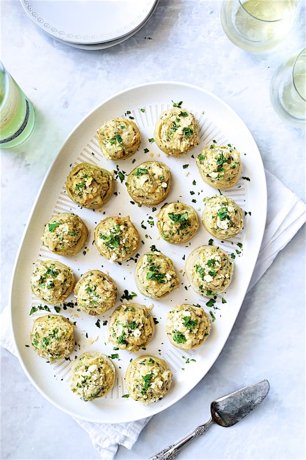 Photo of Deviled Crab-Stuffed Artichoke Bottoms on white oval platter with wine and wine glasses.