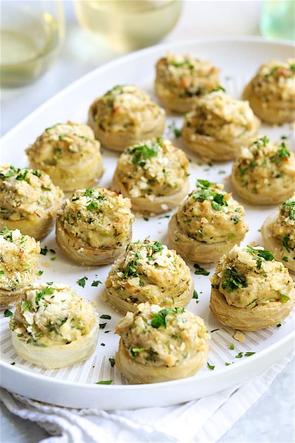 Photo of Deviled Crab Stuffed Artichoke Bottoms on white platter with wine in the background.