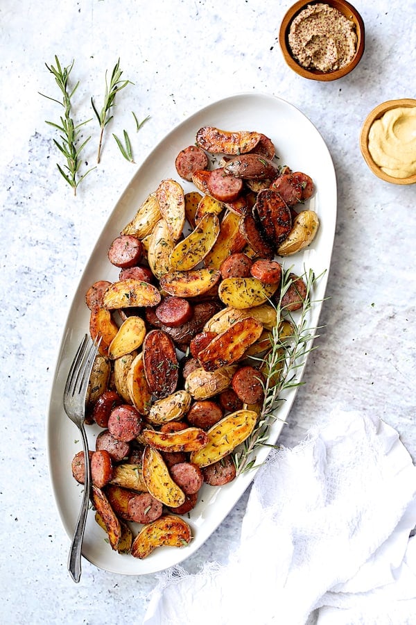 Photo of Duck Fat and Rosemary Roasted Fingerling Potatoes on white oval platter garnished with fresh rosemary.