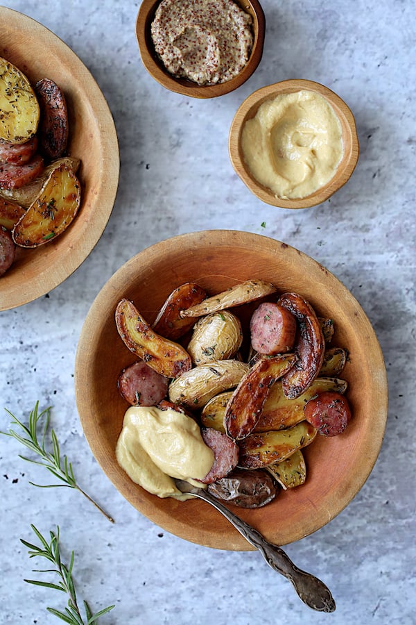 Photo of Duck Fat and Rosemary Roasted Fingerling Potatoes with Sausage served in round wooden bowls with mustard dolloped on.