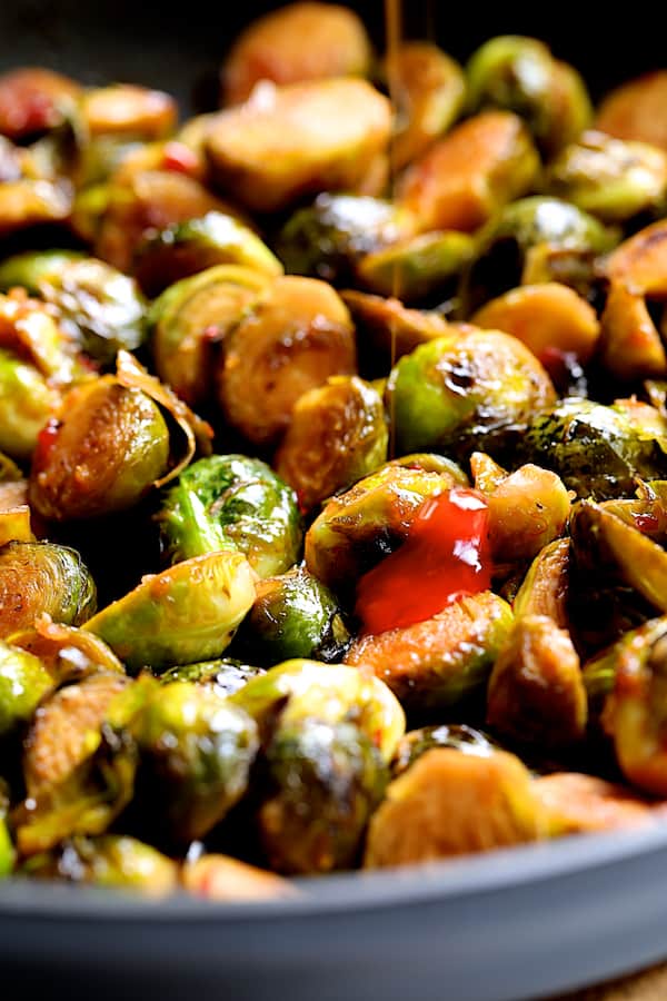Photo of Brussels sprouts in skillet with sweet chili sauce being drizzled on.