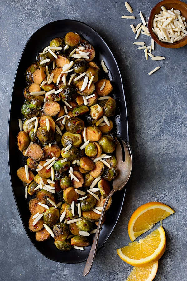 Photo of Pan-Roasted Brussels Sprouts with Thai Sweet Chili Orange Glaze with slivered almonds and orange wedges.