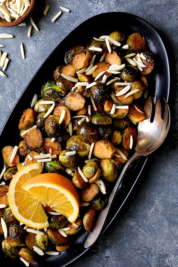 Close-up photo of Pan-Roasted Brussels Sprouts with Thai Sweet Chili Orange Glaze garnished with two orange wedges.