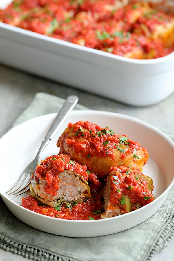 Spicy Italian Stuffed Cabbage - Two of the cabbage rolls in white bowl with one cut in half to expose the inside