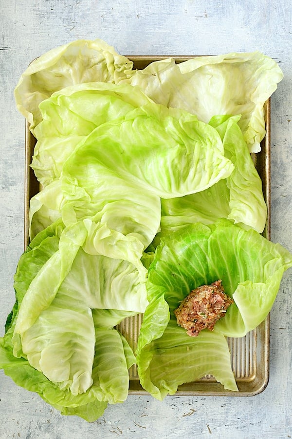 Spicy Italian Stuffed Cabbage - Overhead shot of 12 cabbage leaves on baking sheet with meat filling on one of them