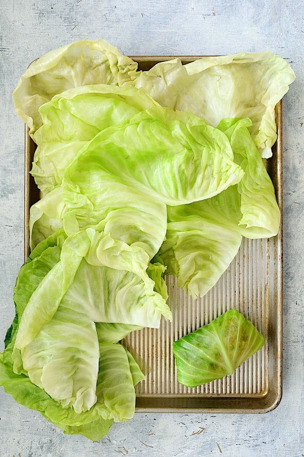 Spicy Italian Stuffed Cabbage - Overhead shot of cabbage leaves on baking sheet with one fully rolled