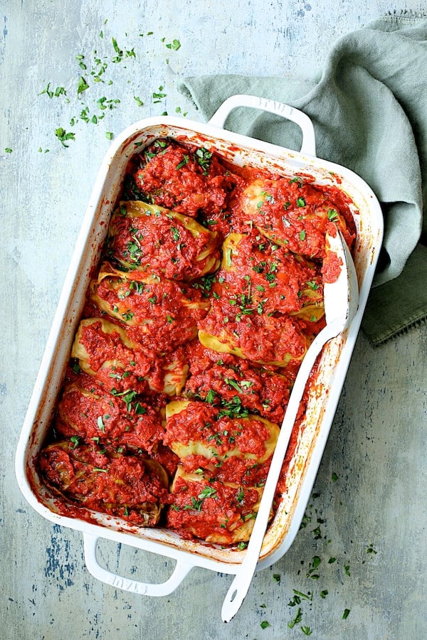 Spicy Italian Stuffed Cabbage - Overhead shot of stuffed cabbage with pan on an angle sprinkled with parsley with blue-green towel on blue-green background