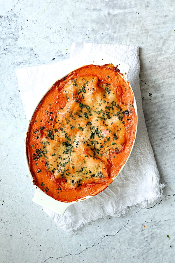 Photo of baked Shrimp Scallop and Artichoke Lasagna in white oval baking dish on white towel.