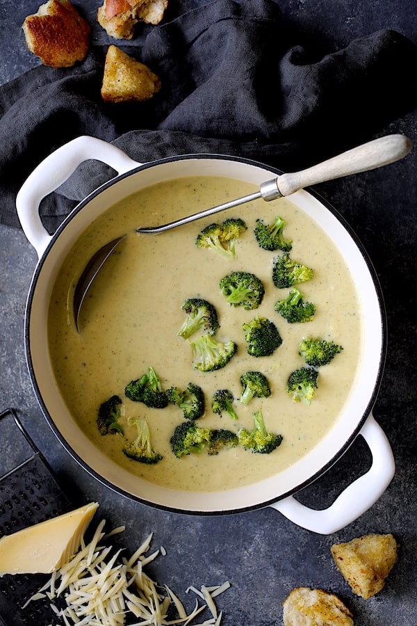 Broccoli Gruyere Soup with Torn Garlic Croutons - Overhead shot of soup in white Dutch oven on dark blue background