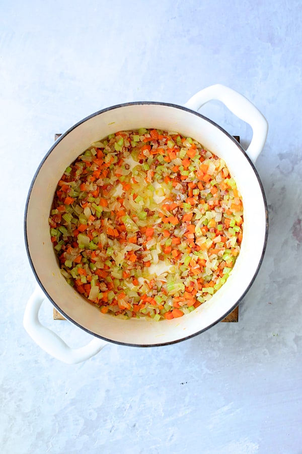 Photo of onion, carrot and celery being browned in white Dutch oven.