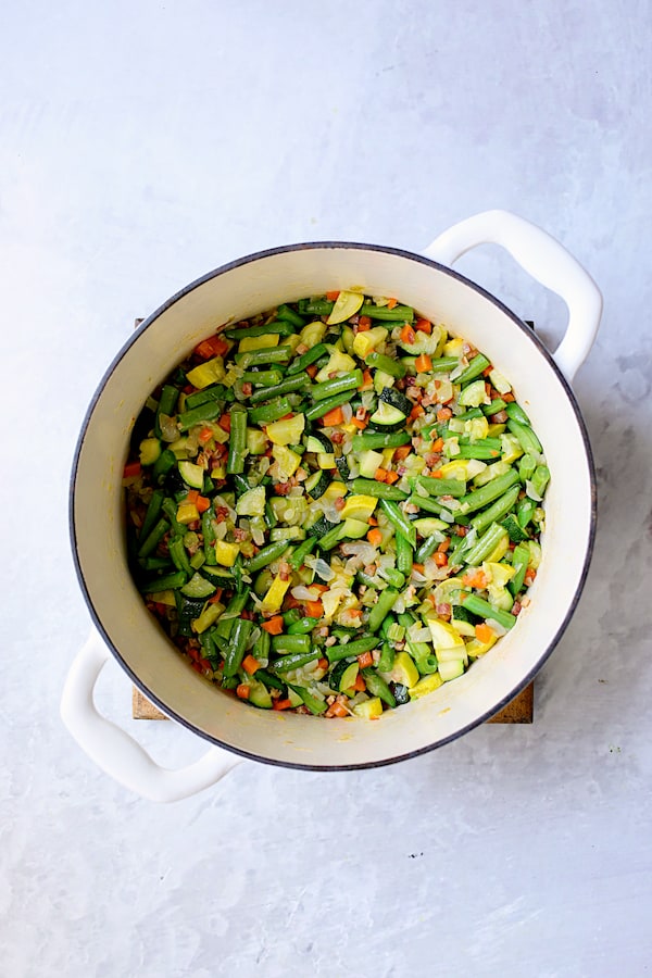 Photo with zucchini, yellow squash and green beans in white Dutch oven.
