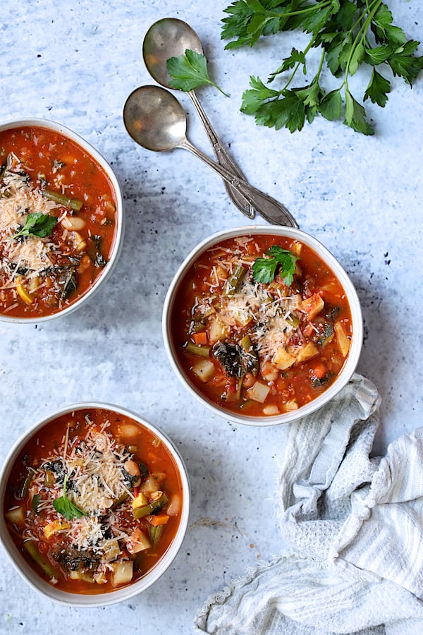 Photo of three servings of Italian Vegetable Stew in white bowls garnished with grated Parmesan cheese and parsley.