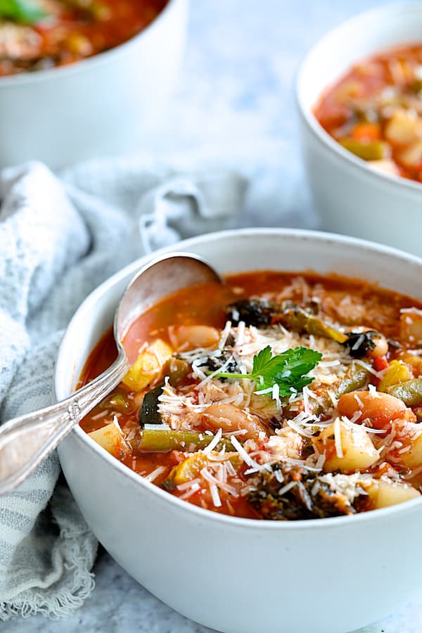 Close-up photo of one serving of Italian Vegetable Stew in white bowl garnished with Parmesan cheese and parsley.