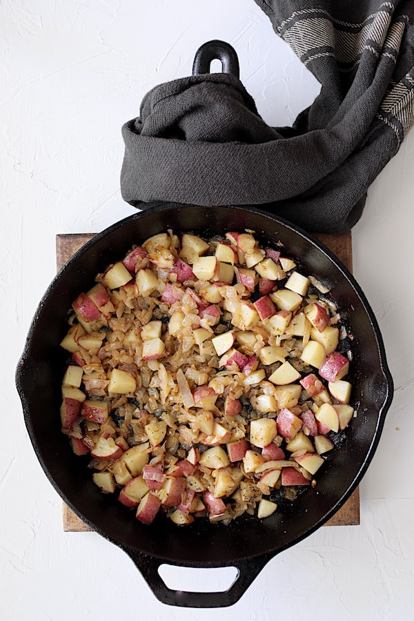 Photo of onions and potatoes cooking in cast iron skillet.