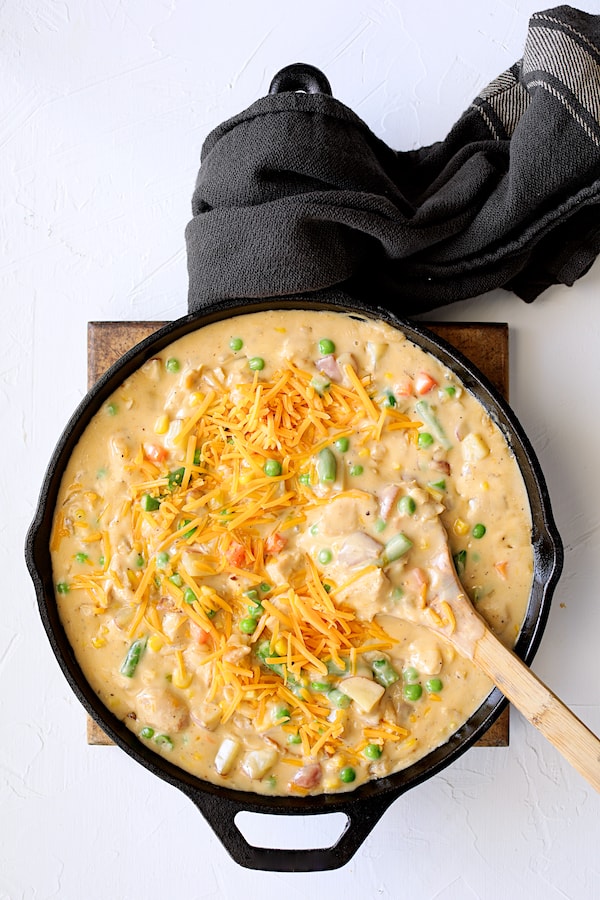 Photo of the chicken pot pie filling with cheese being stirred in with wooden spoon.