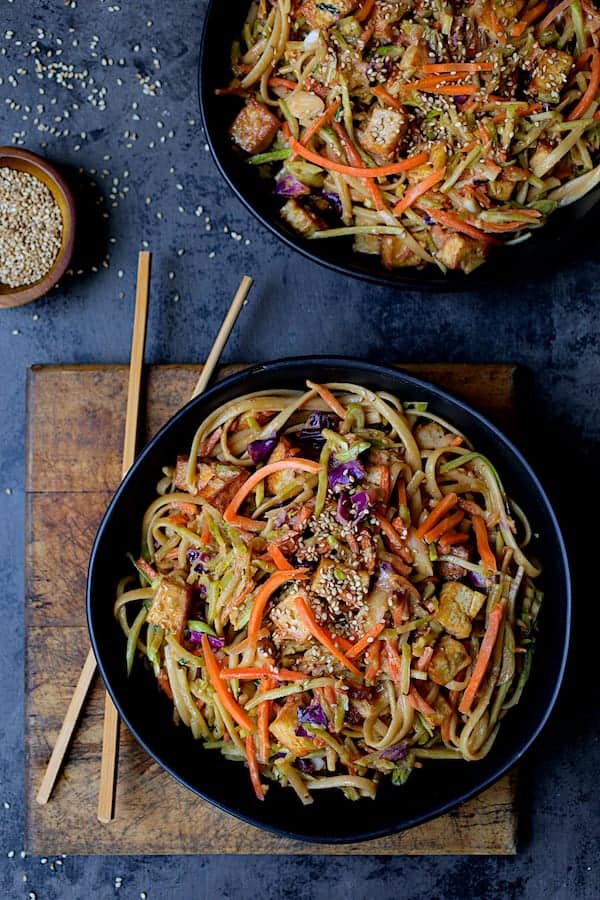 Thai Sesame Noodles with Tofu and Vegetables - Overhead hero shot of dish in black bowls on dark blue background