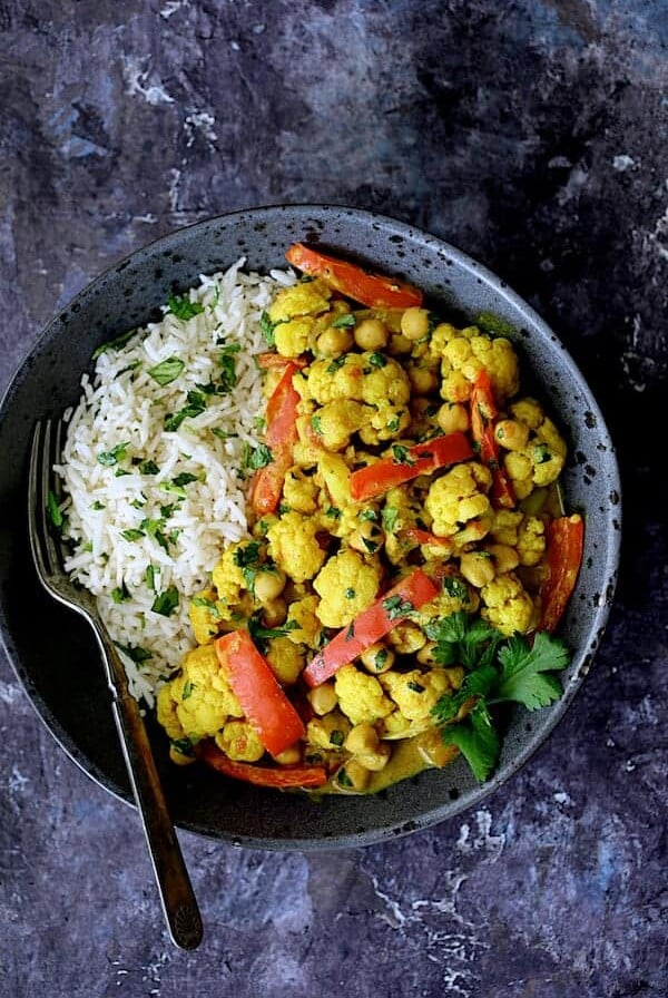 One serving of Vegan Indian Cauliflower and Chickpea Curry with basmati rice in a gray bowl.