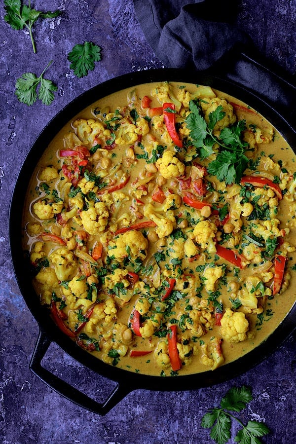Photo of Vegan Indian Cauliflower and Chickpea Curry in cast iron skillet on blue background.