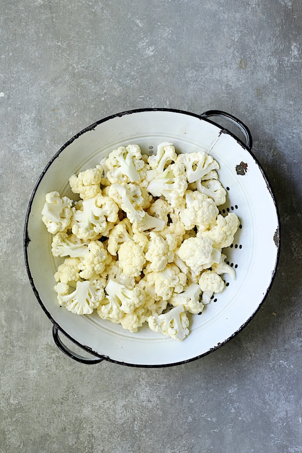 Photo of raw cauliflower in white distressed colander on gray background.