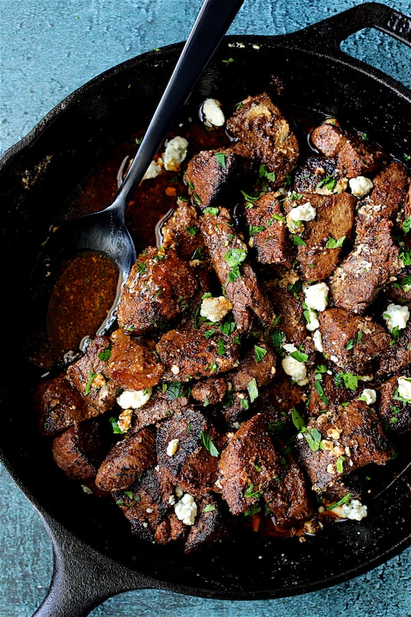 Buttery Blackened Steak Bites with Gorgonzola - Cheese being added to steak bites in cast iron skillet
