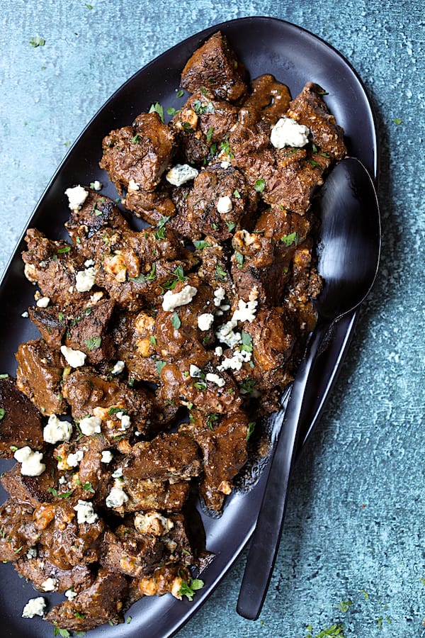 Buttery Blackened Steak Bites with Gorgonzola - Close-up shot of steak bites on black platter with more cheese added
