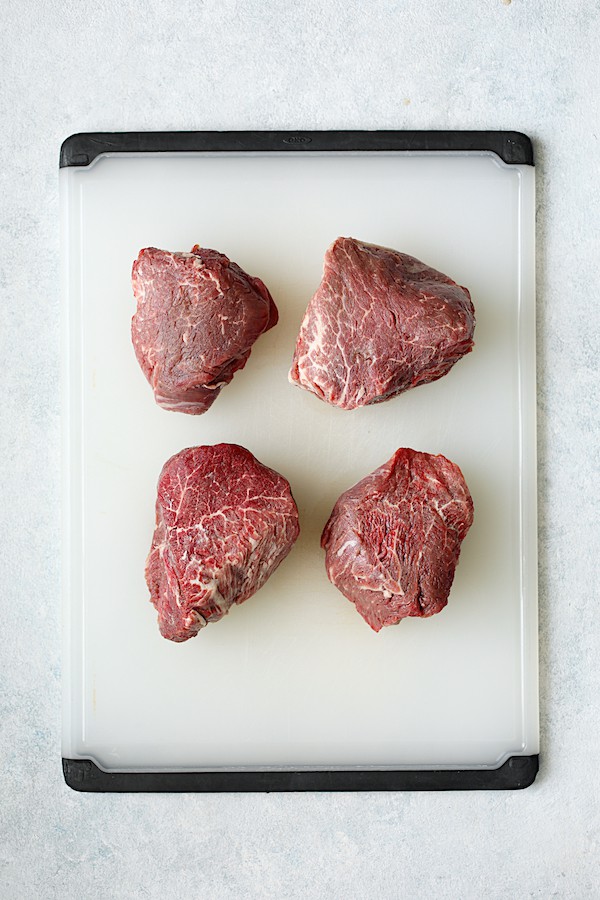 Overhead shot of four steaks on white cutting board