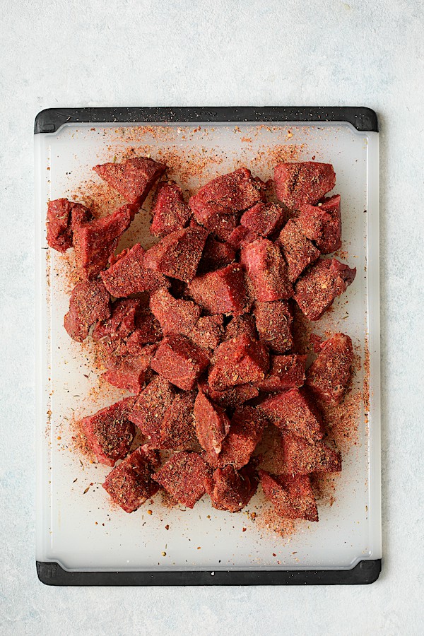 Overhead shot of steak bites on white cutting board dredged in blackening mix