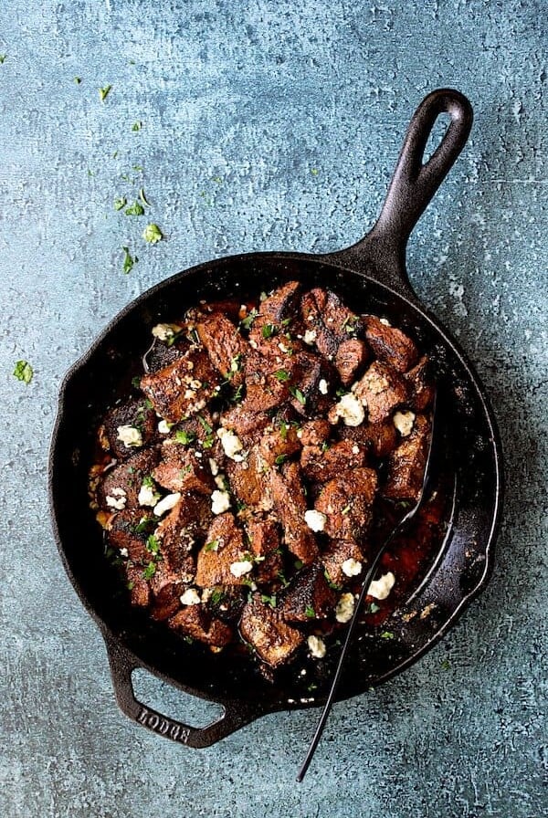 Buttery Blackened Steak Bites with Gorgonzola in cast iron skillet with serving spoon.