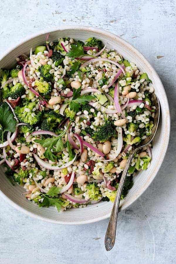 Photo of Lemony Broccoli, Barley and Bean Salad in white serving bowl with serving spoon.
