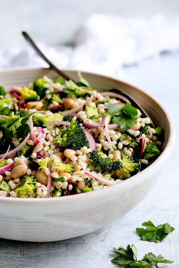 Close-up photo of Lemony Broccoli, Barley and Bean Salad in white serving bowl with serving spoon.