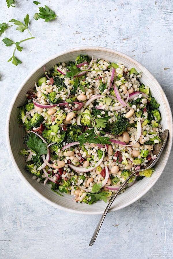Photo of Lemony Broccoli, Barley and Bean Salad in white serving bowl garnished with parsley.