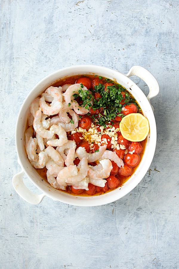 Photo of shrimp, parsley, garlic and lemon added to roasted tomatoes in white baking dish.
