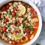 Spicy Baked Shrimp with Tomatoes and Feta Cheese in round white baking dish garnished with parsley and lemon.